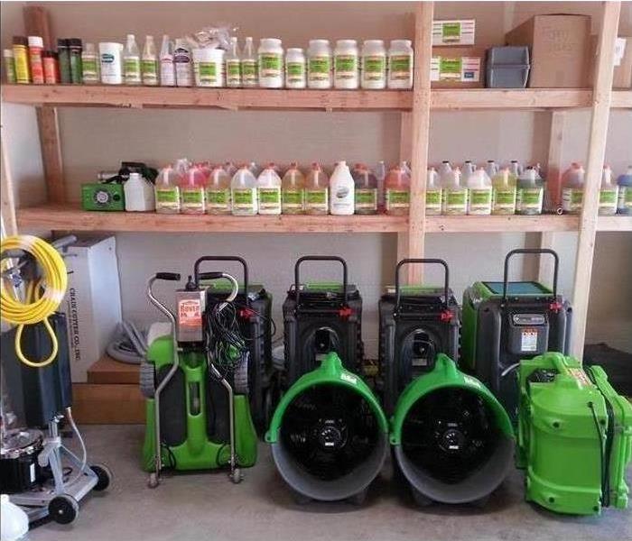 Shelves with rows of cleaning products on them and SERVPRO equipment in front.
