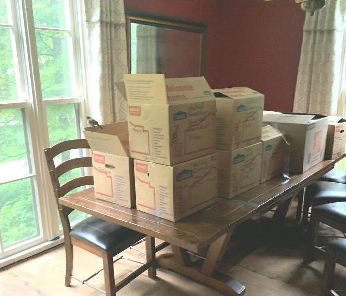 A pile of moving boxes stacked on a dining room table after a water loss.