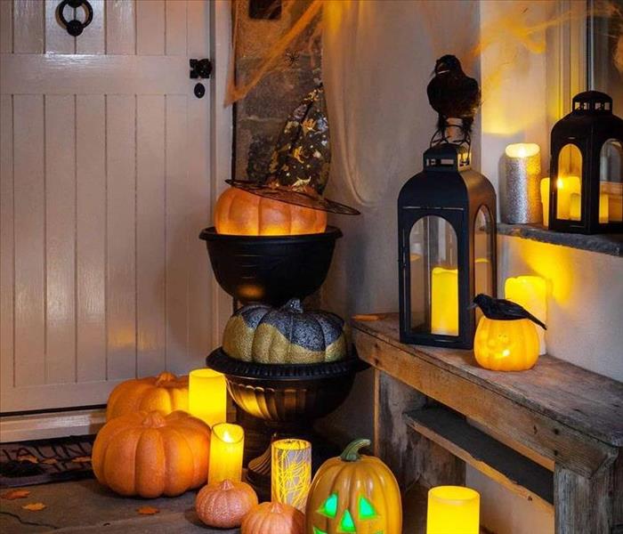 A Halloween display set up on a front porch consisting of battery-operated candles, pumpkins, leaves, cauldrons, and a crow.